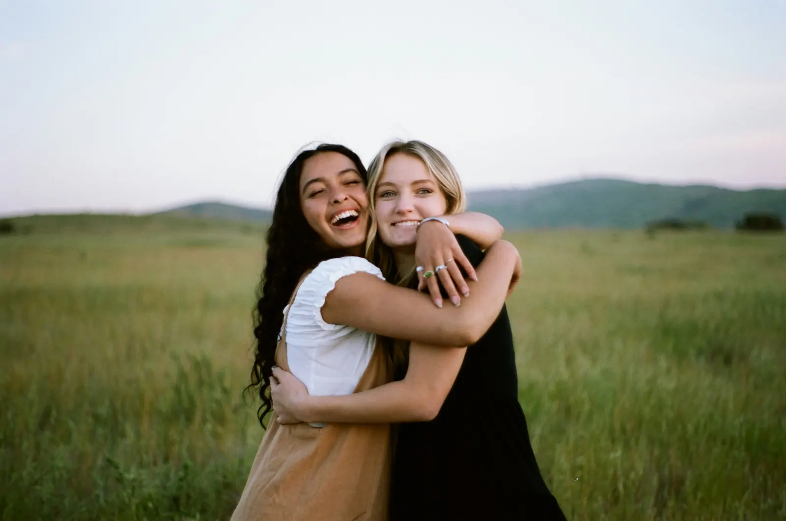 Two friends hugging and laughing in a field